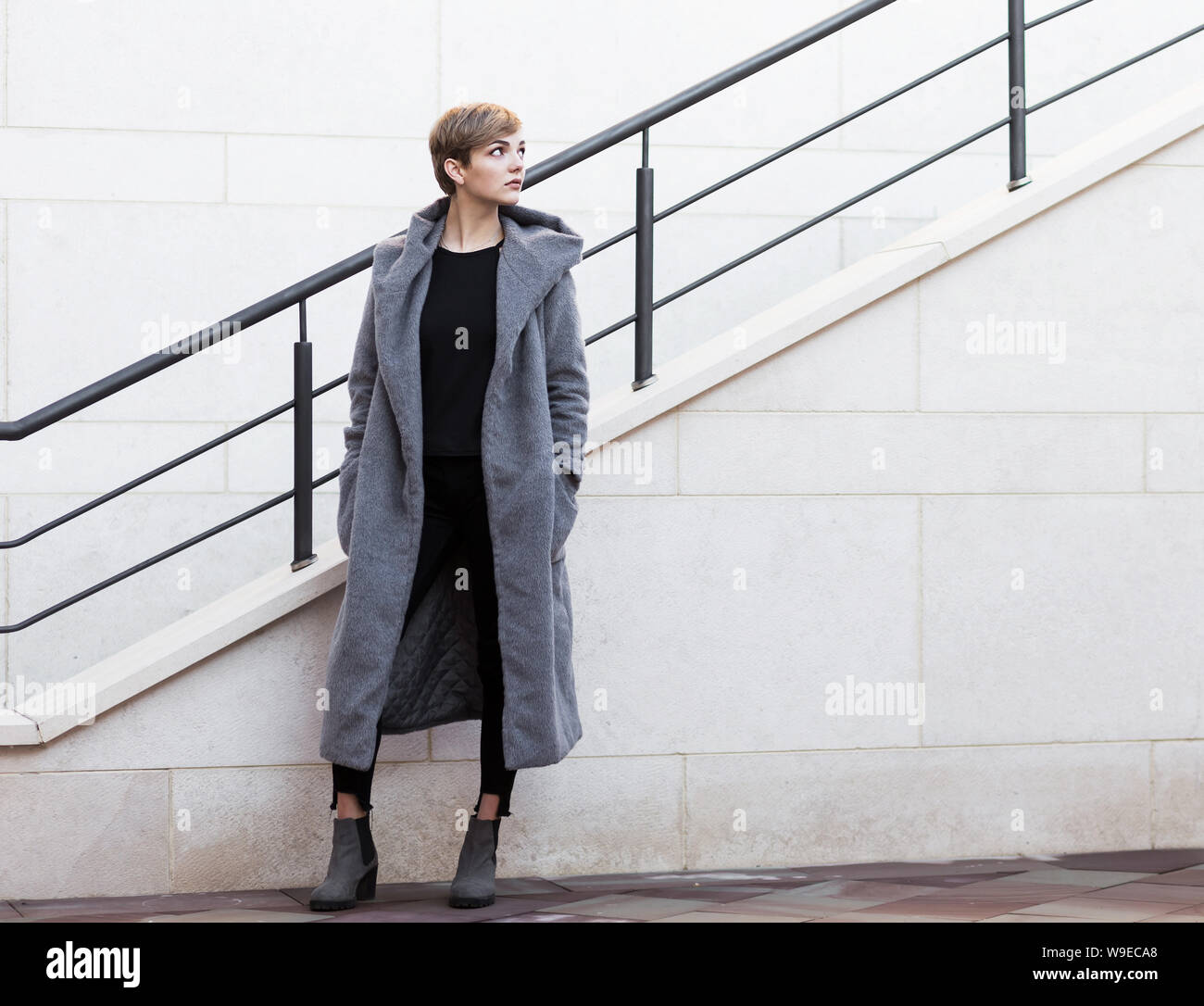 Stilvolle Frau im grauen Mantel schaut oben auf der Treppe Hintergrund Stockfoto
