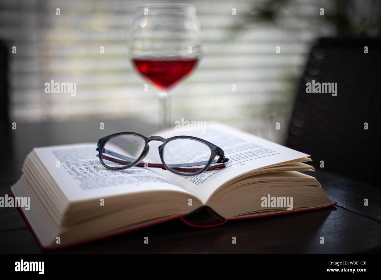 Ein paar Gläser liegt auf einem offenen Buch und im Hintergrund ist ein Glas Wein Stockfoto