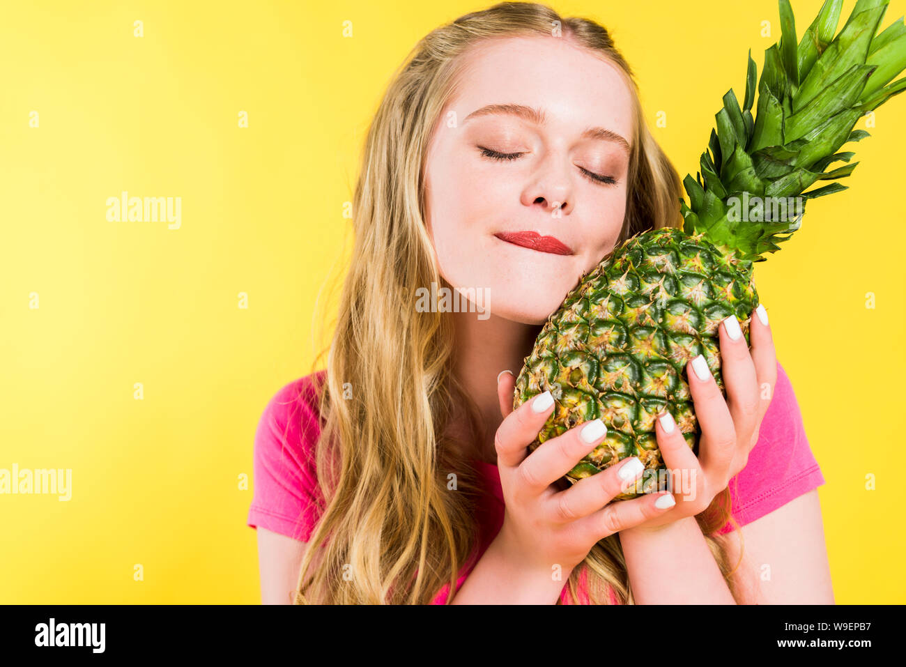 Schöne Mädchen, Beißen, Lippe und posieren mit Ananas isoliert auf Gelb Stockfoto