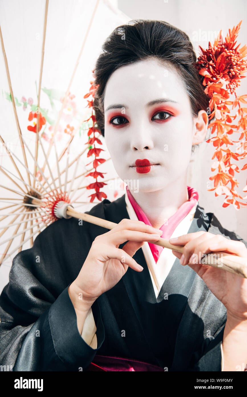 Wunderschöne Geisha mit roten und weißen Make-up, Regenschirm in der Sonne Stockfoto