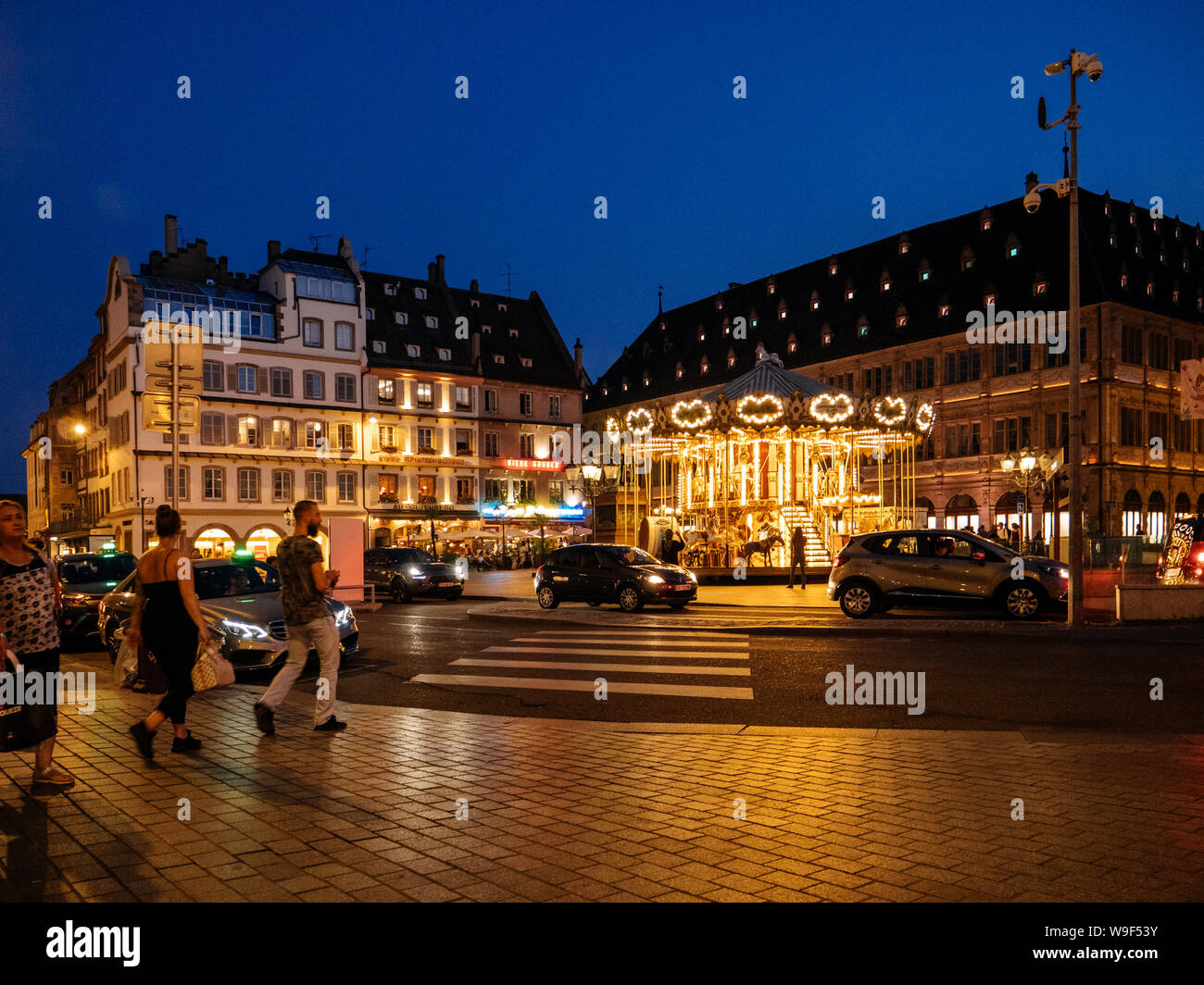 Straßburg, Frankreich - 25.August 2017: Fußgänger zu Fuß in der Dämmerung am Place Gutenberg mit Merry go round in Betrieb, Autos in der Tiefgarage parken und Taxis warten auf Kunden Stockfoto