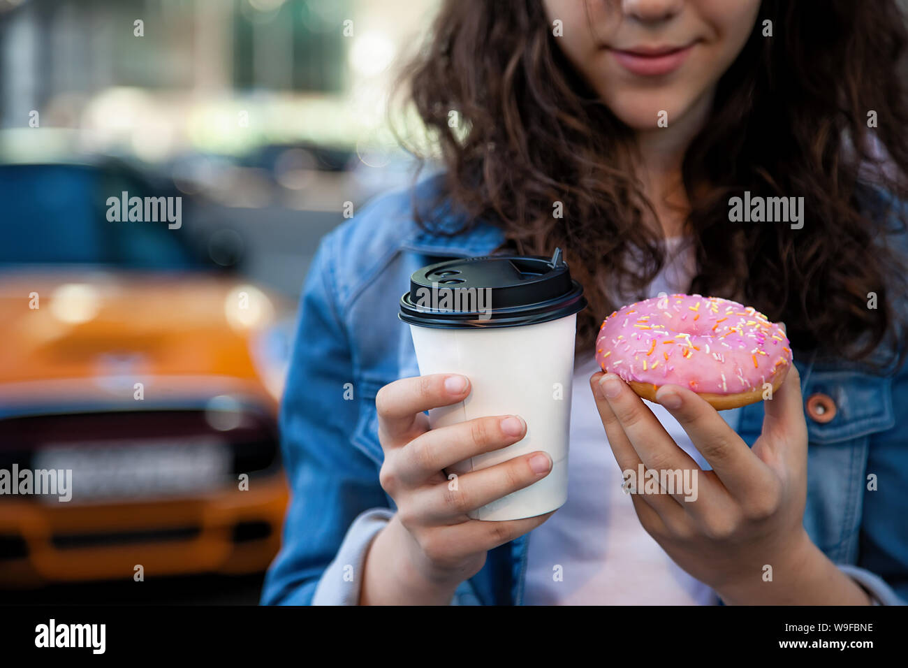 Hände halten ein rosa Donut und Kaffee auf dem Hintergrund einer geschäftigen Metropole. Stockfoto