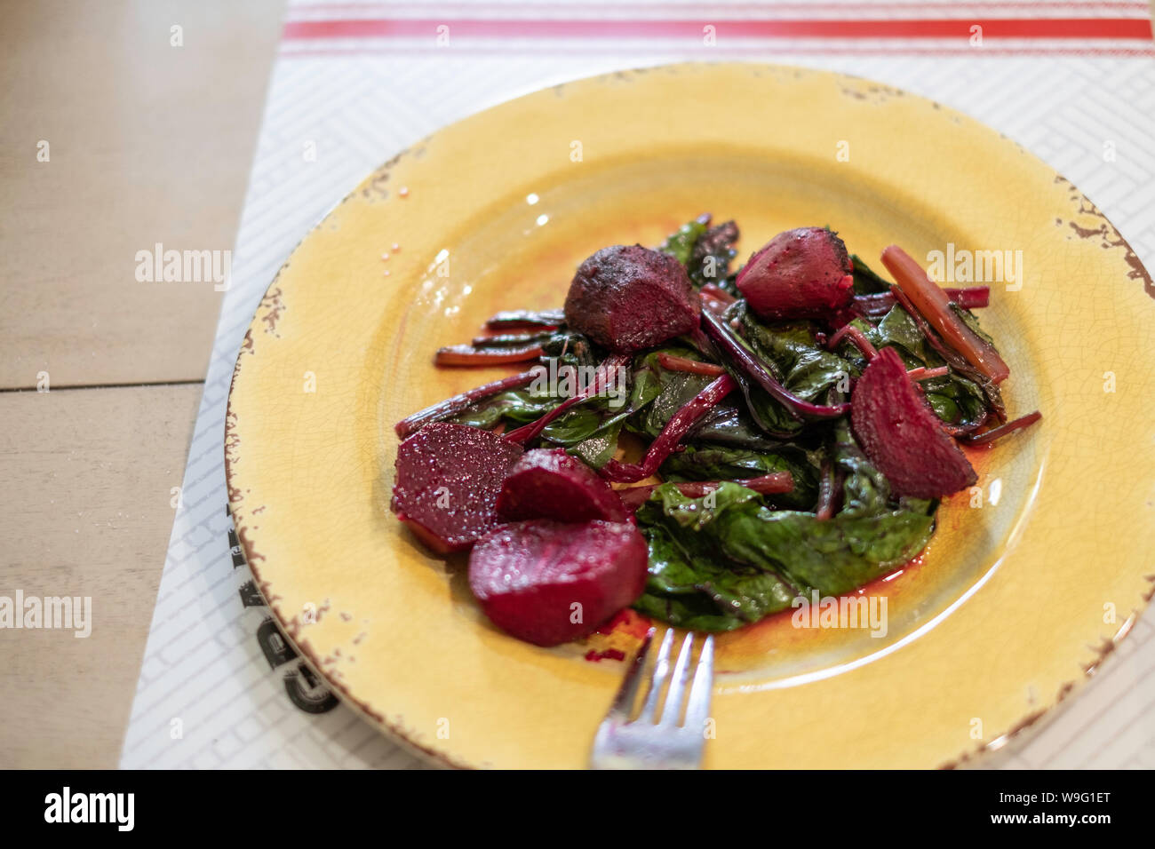 Heiße, frisch gekochte Rüben oder Rote Bete mit Blattspitzen, gewürzt mit Olivenöl und Knoblauch auf einem gelben Teller. Stockfoto
