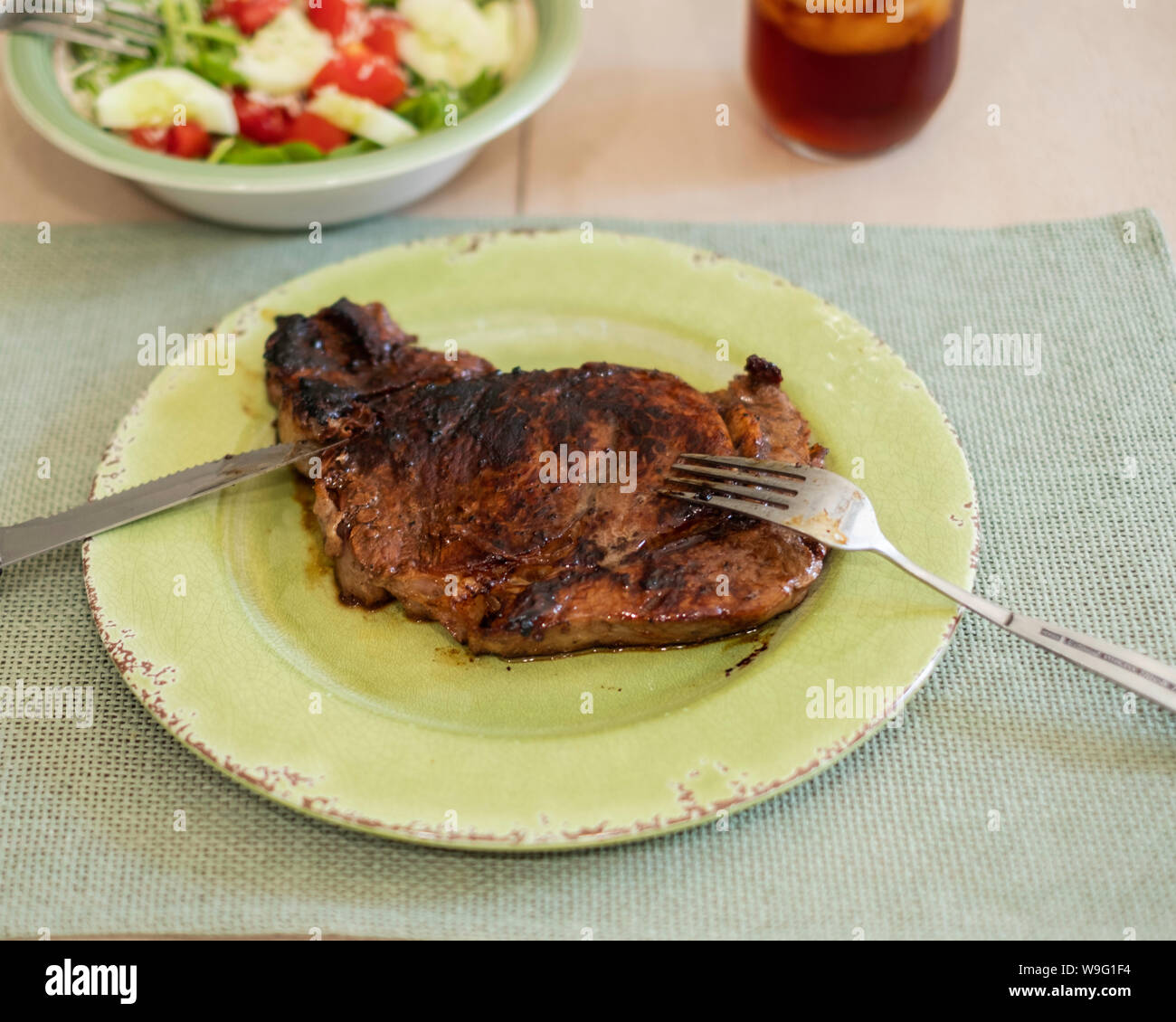 Ribeye Steak, gegrillt, serviert auf einem grünen Platte und Tischset. Utensilien und einem gemischten Salat. Stockfoto