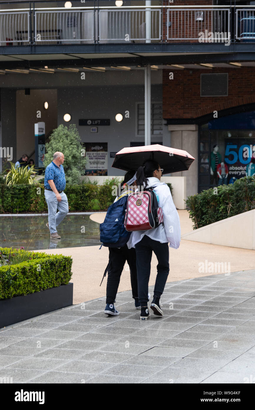 Zwei junge Mädchen unter einem Sonnenschirm im Regen in einem Einkaufszentrum Stockfoto