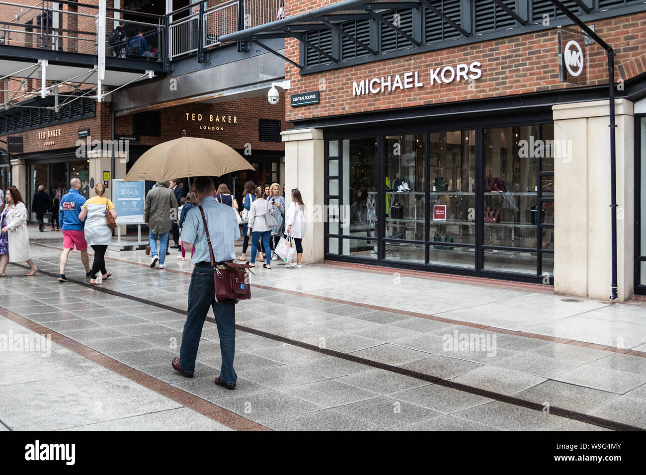 Ein Mann Unterschlupf vor dem Regen unter einem Sonnenschirm in einem Einkaufszentrum Stockfoto