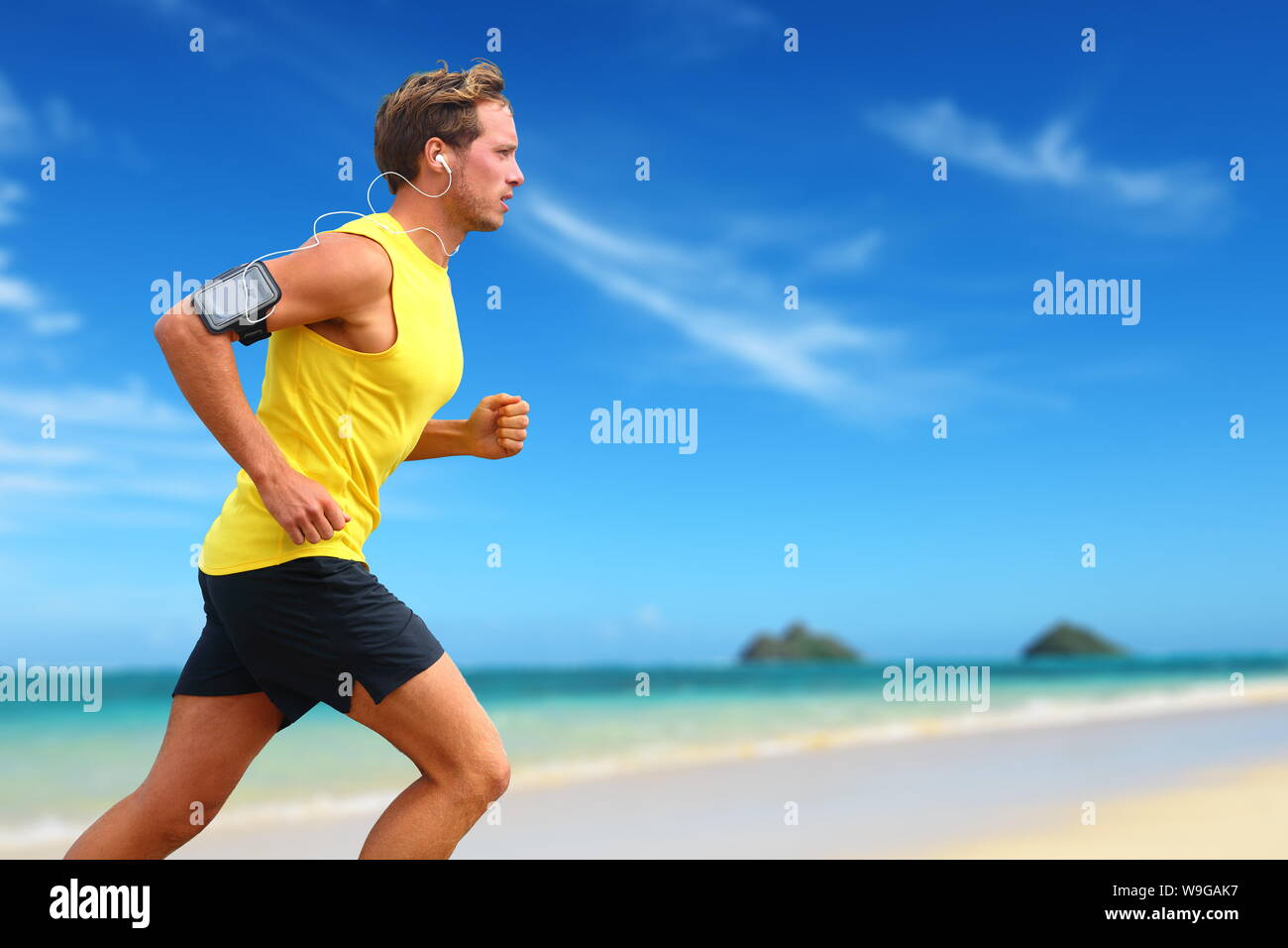 Runner hören Smartphone Musik laufen am Strand. Lanikai, Oahu, Hawaii, USA. Männliche Athlet joggen am Ocean Beach oder am Wasser, Arbeiten mit Smart Phone App gerät und Ohrhörer im Sommer. Stockfoto