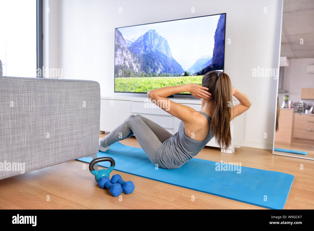 Home Training - Frau Ausübung vor einem Flachbildschirm mit einem fitnessprogramm oder Trainieren während einer TV-Show liegen auf einem Yoga Matte vor dem Sofa im Wohnzimmer eines Hauses oder einer Wohnung. Stockfoto