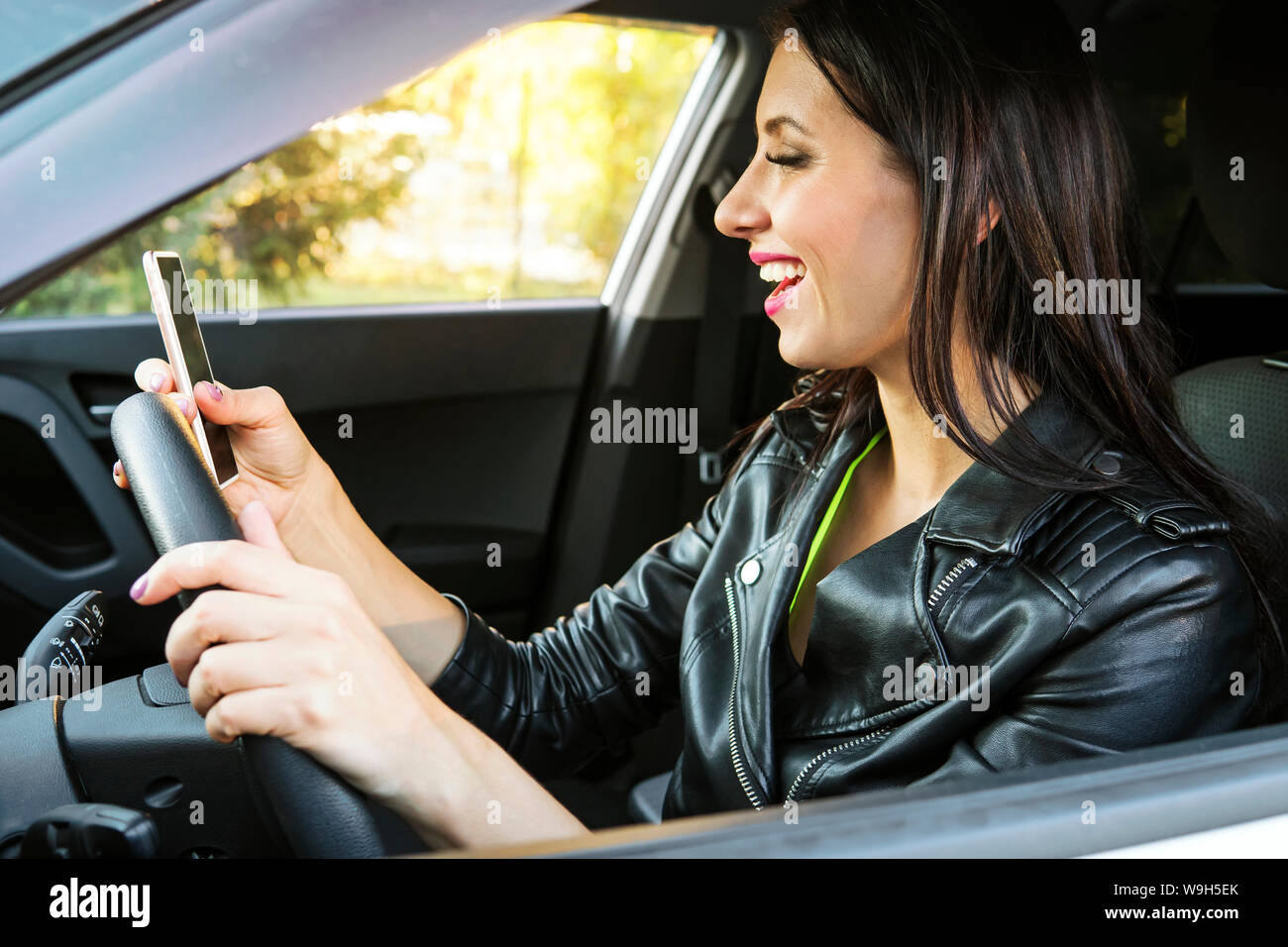 Glücklich lächelnde Frau mit Ihrem Smart Phone in einem Auto sitzen. Weibliche Treiber Lachen lesen Nachricht und Chatten in Mobile. Mädchen schaut Sie Stockfoto