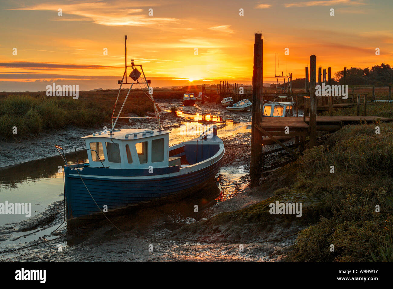 Geerdete Boote warten auf die Flut an Thornham in der Nähe von Hunstanton Norfolk mit der aufgehenden Sonne im Hintergrund zu kommen Stockfoto