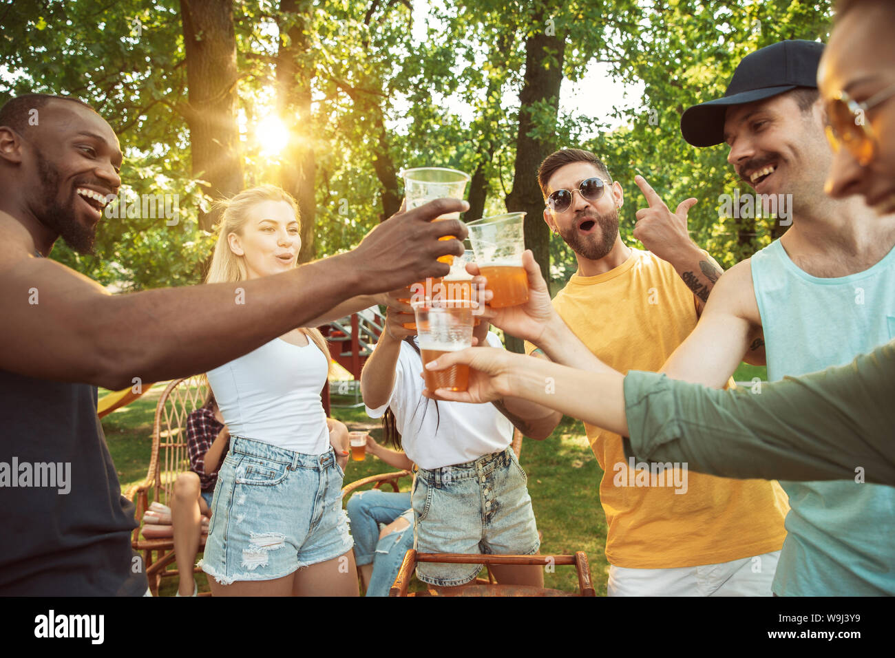 Gruppe der glücklichen Freunde in Bier und Grill Party im sonnigen Tag. Zusammen Ruhen im Freien in einer Waldlichtung oder Hinterhof. Feiern und Entspannen, Laughting. Sommer Lifestyle, Freundschaft Konzept. Stockfoto