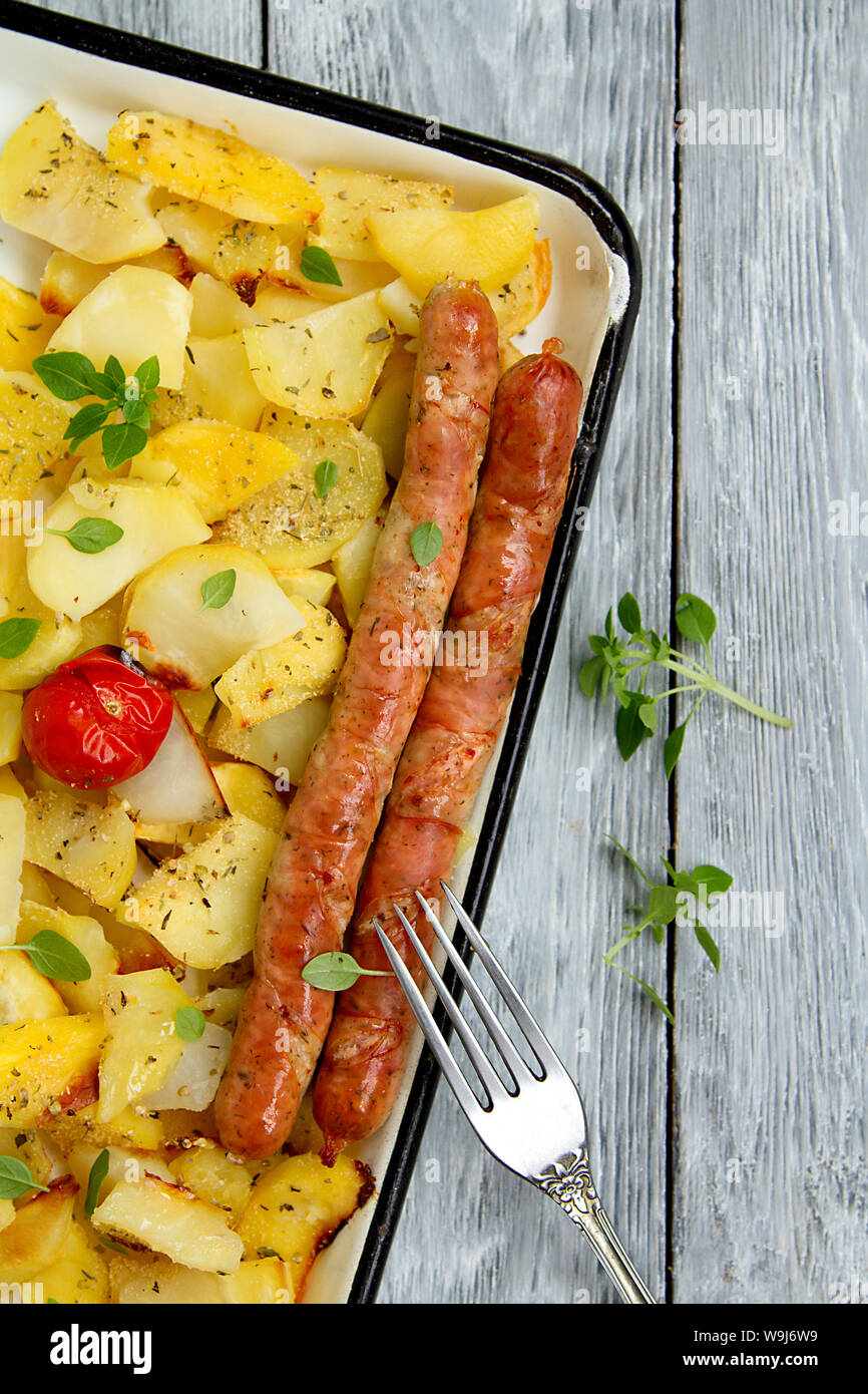 Tasy gebackene Kartoffelscheiben mit gebratenen München Würstchen mit Basilikumblätter auf ein Backblech Stockfoto