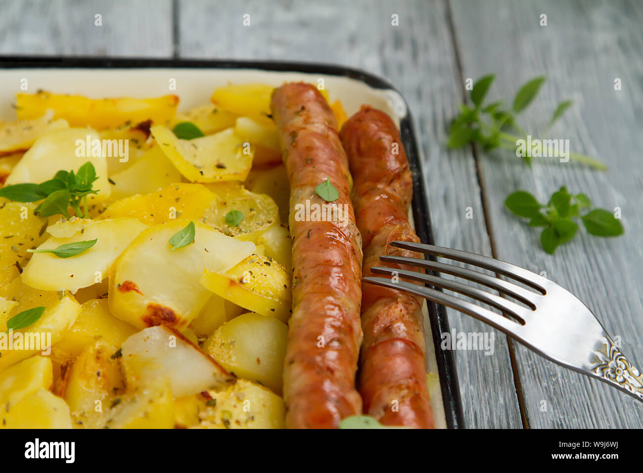 Tasy gebackene Kartoffelscheiben mit gebratenen München Würstchen mit Basilikumblätter auf ein Backblech Stockfoto