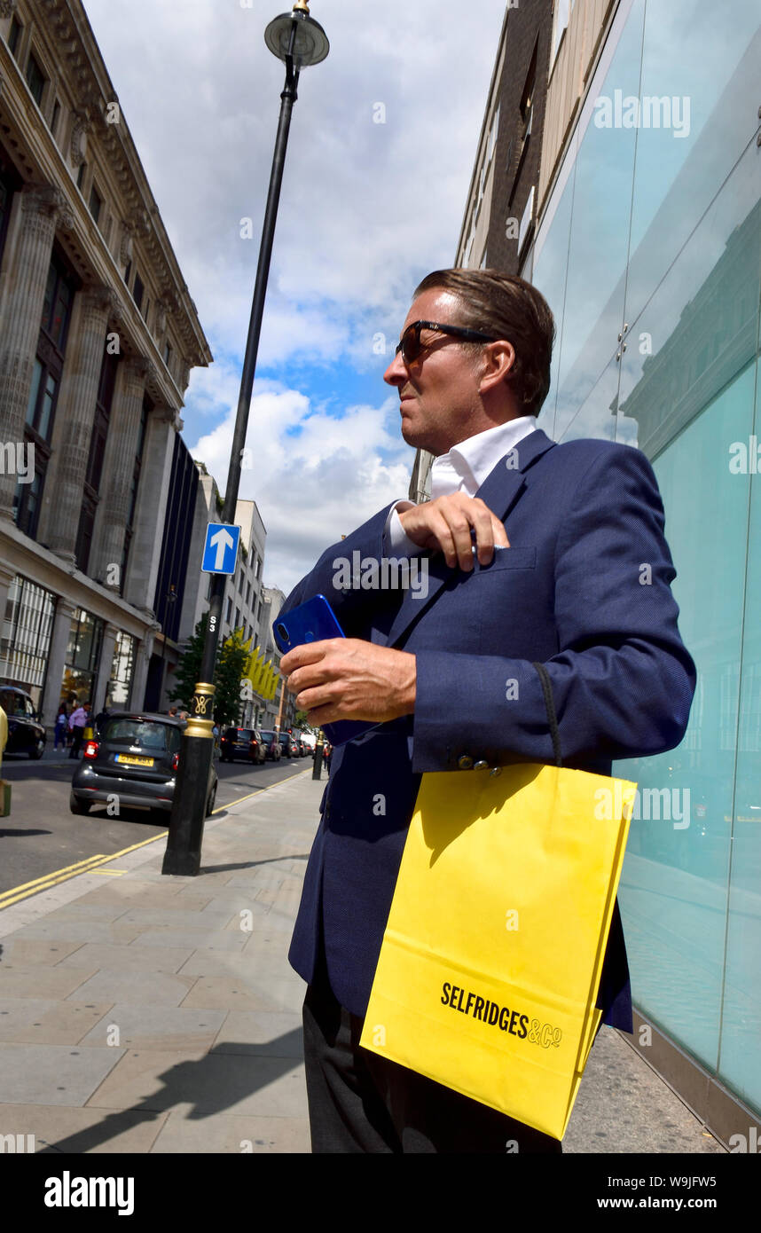 London, England, UK. Gut braungebrannte Mann mit Selfridges Tragetasche gekleidet Stockfoto