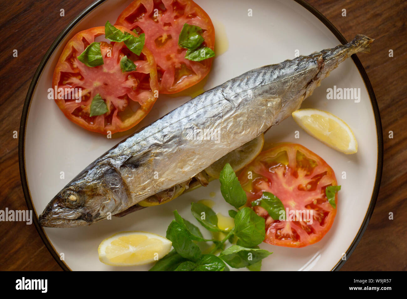 Eine Makrele Scomber scombrus, dass gekocht worden en Papillote hat und serviert mit in Scheiben geschnittenen Tomaten, Basilikum, Olivenöl und Zitrone Keile. Es war gefüllt mit Stockfoto