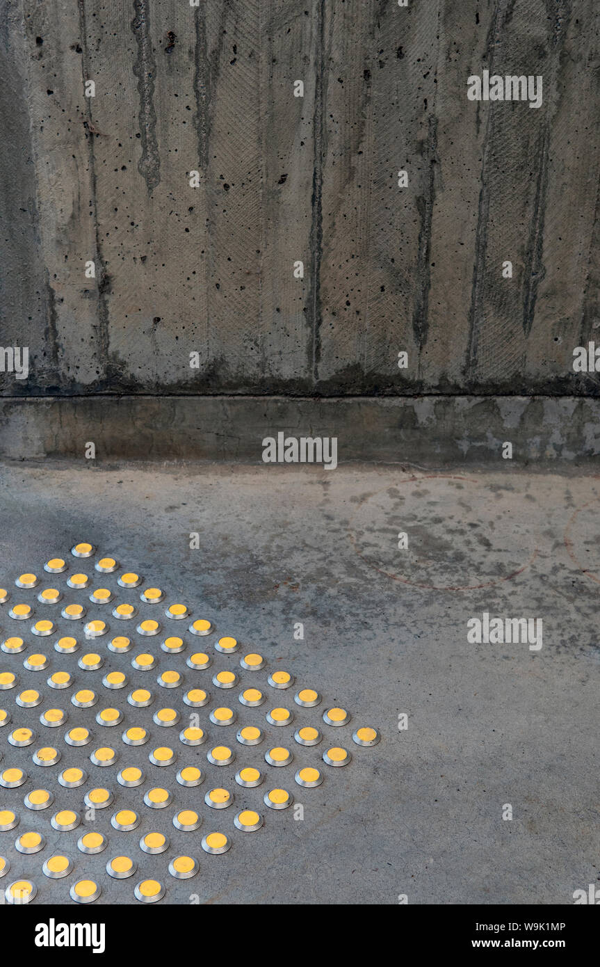 Gelbe taktile Pflaster Warnung Beulen neben einem Brutalist Betonwand Stockfoto