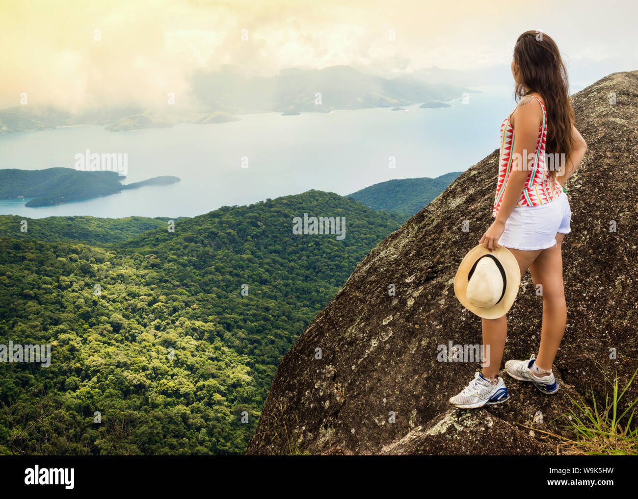 Junge Frau mit Blick auf die grüne Küste (Costa Verde) von Papapagaio Gipfel (Pico do Papagaio) auf der Insel Ilha Grande, Rio de Janeiro, Brasilien Stockfoto