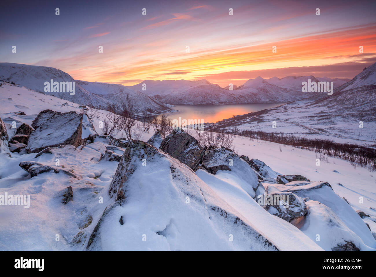 Gefrorene Meer umgeben von Schnee, eingerahmt vom orange Himmel bei Sonnenuntergang, Torsken, Senja, Troms County, Arktis, Norwegen, Skandinavien, Europa Stockfoto