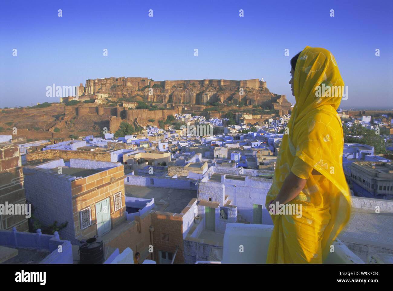 Eine Frau in einem gelben Sari mit Blick auf die "Blaue Stadt" und Fort, Jodhpur, Rajasthan, Indien, Asien Stockfoto