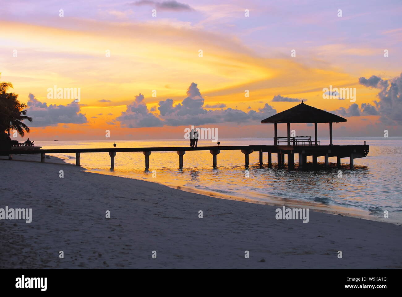 Paar am Steg mit Blick auf den Sonnenuntergang, Malediven, Indischer Ozean, Asien Stockfoto