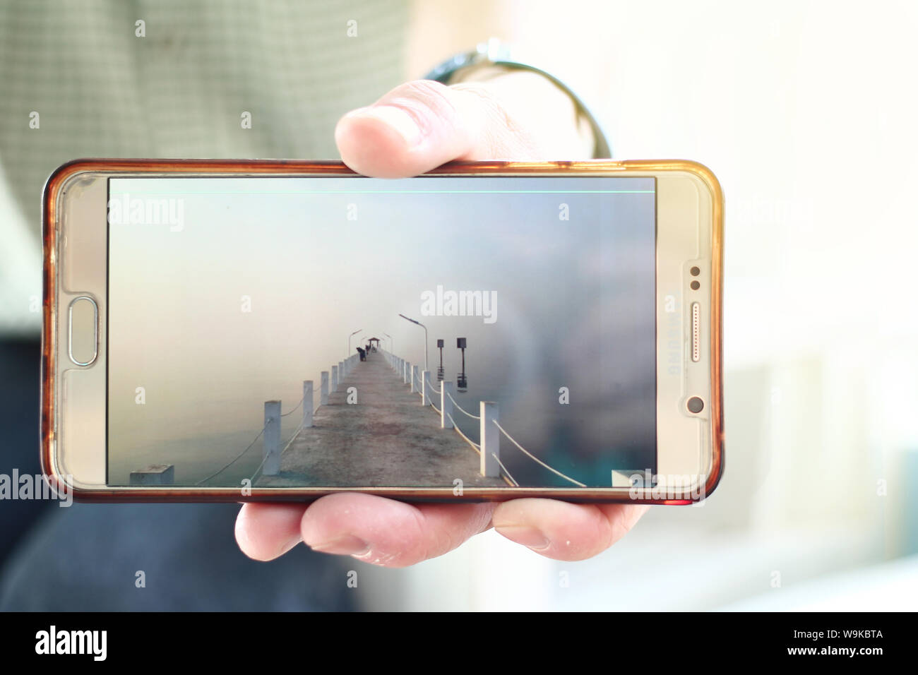 Mit der linken Hand halten Handy Foto der kleinen Fischer Hafen und Meer in Morgen anzeigen zu legen. Stockfoto