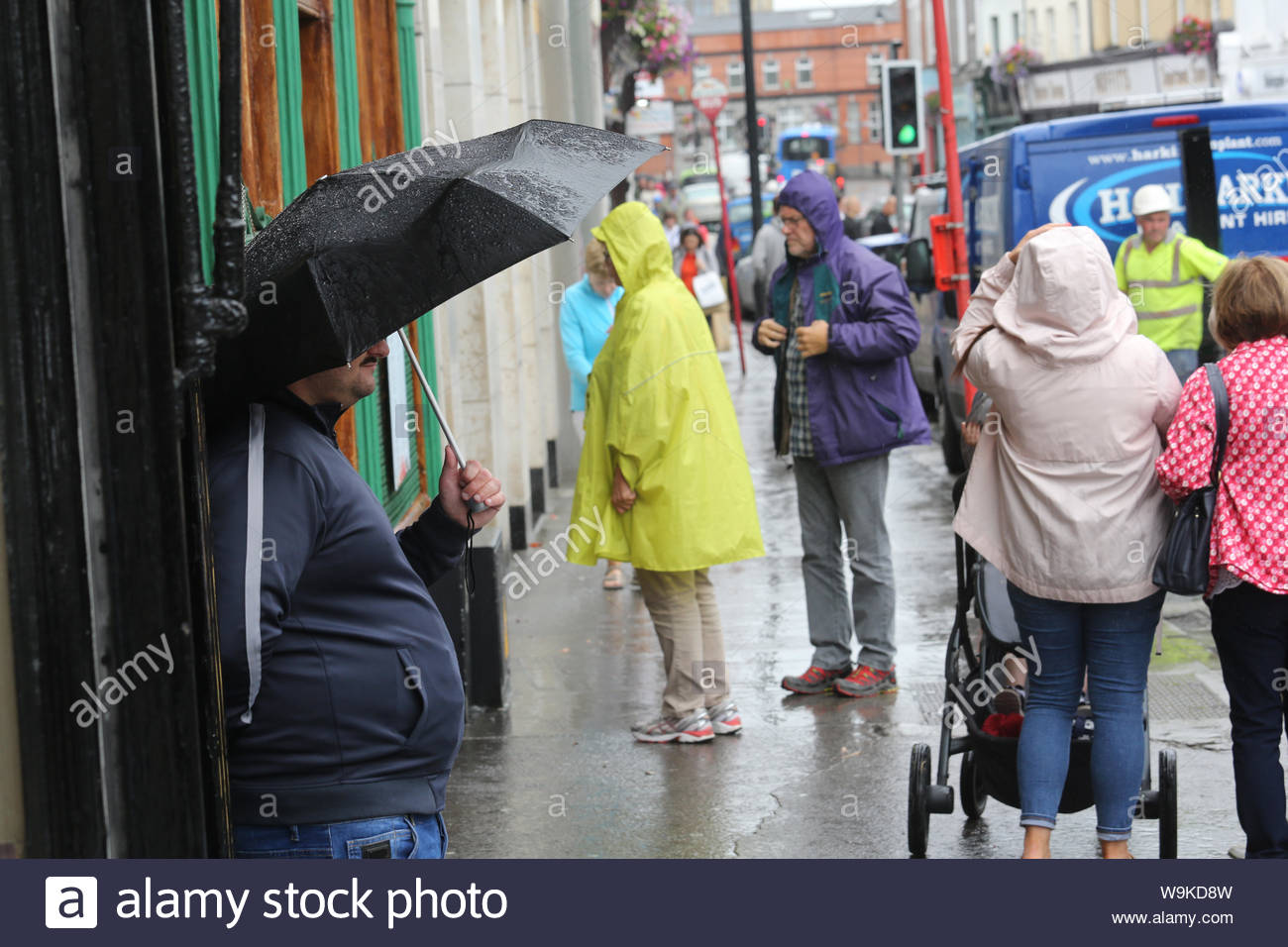 Ein Mann Unterstände unter einem Sonnenschirm während einer schweren Dusche im Zentrum von Sligo, Irland, heute Nachmittag. Die Prognose für die weitere wechselhafter Witterung in den nächsten Tagen. Stockfoto