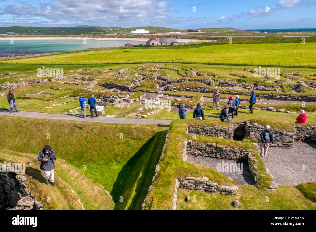 Touristen, die in der Nordischen Siedlung ausgegraben Jarlshof in der Nähe von Sumburgh Head im Süden von Mainland, Shetland. West Voe von sumburgh im Hintergrund. Stockfoto