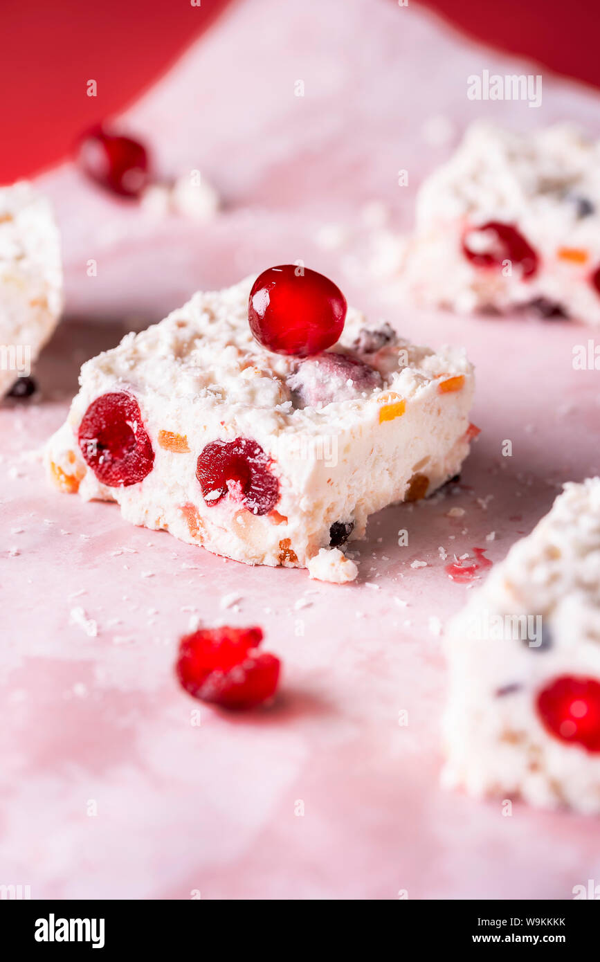 Stück der Australischen süß, eine weiße Weihnachten Kuchen mit Kokos und getrockneten Kirschen, auf Backpapier. Nahaufnahme der Winter Dessert. Traditionelle Weihnachten Kuchen Stockfoto