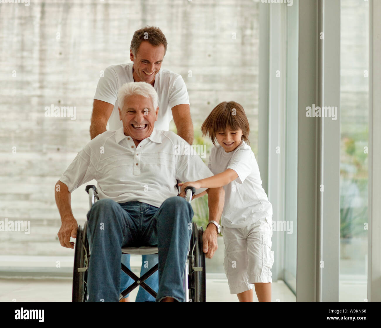 Ältere Menschen, der im Rollstuhl geschoben, von seinen erwachsenen Sohn und seinem Enkel. Stockfoto