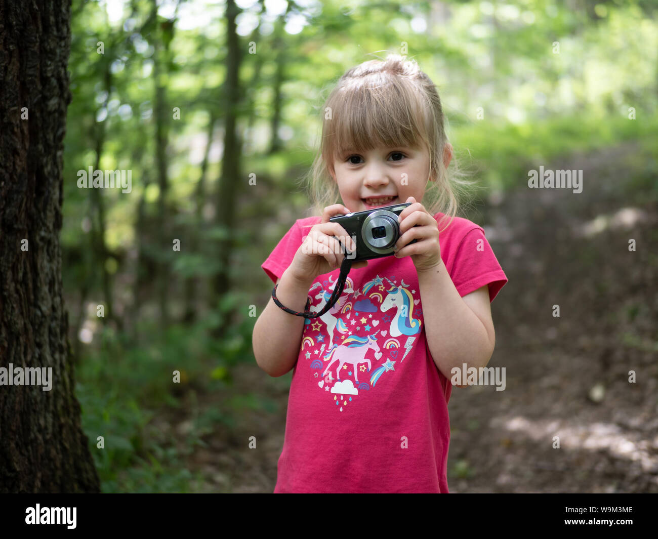 Blond, glücklich, 4-jähriges Mädchen im Wald hält eine Kamera und ein Lächeln Stockfoto