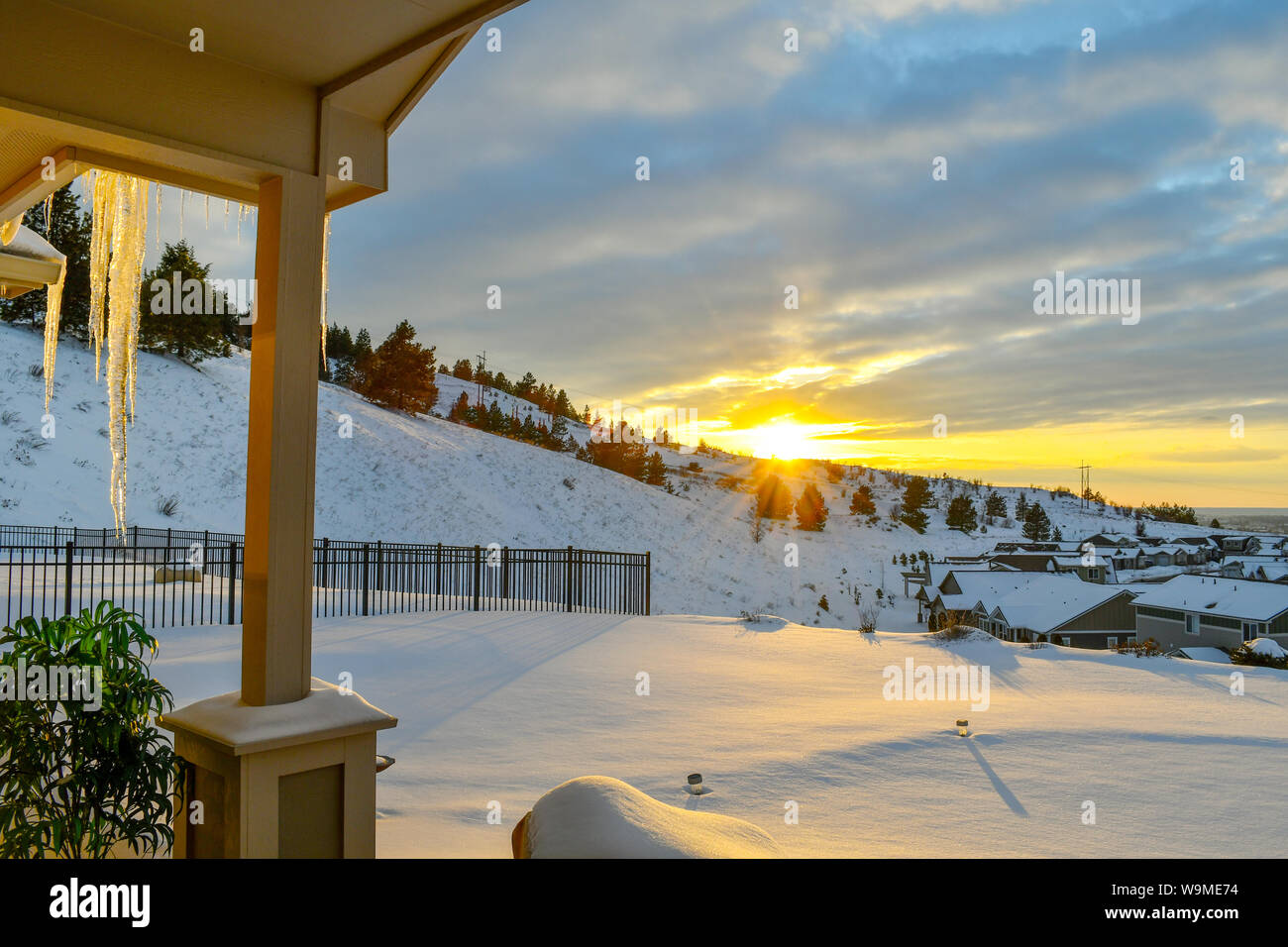 Blick von einer überdachten Deck wie die untergehende Sonne beleuchtet einen großen Eiszapfen auf einem verschneiten Hügel oberhalb einer Nachbarschaft Unterteilung in Spokane Washington Stockfoto