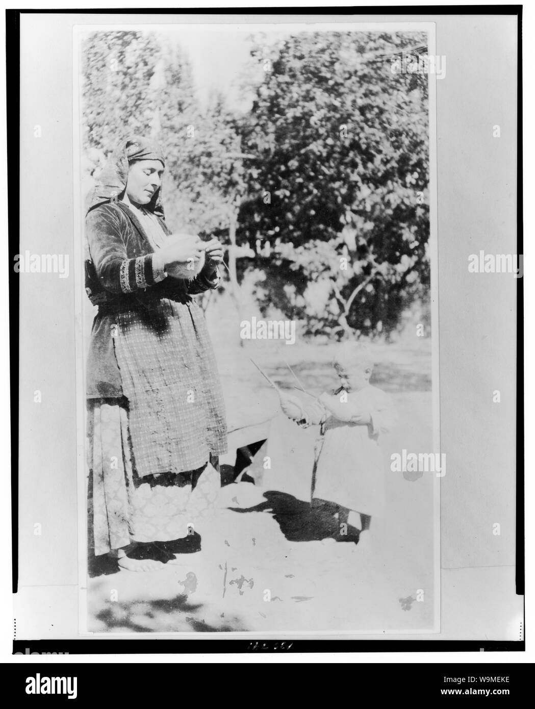 Armenischen Kinder beginnen, sich an einem frühen Alter abstrakte nützlich zu machen: Armenische Frau mit Kugel aus Garnen, als Kind hält zwei Spindeln. Stockfoto