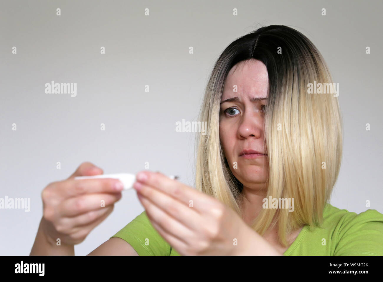 Verärgert Frau sieht digitales Thermometer in den Händen. Die Messung der Körpertemperatur, Fieber, Erkältung und Grippe, Krankheit Stockfoto