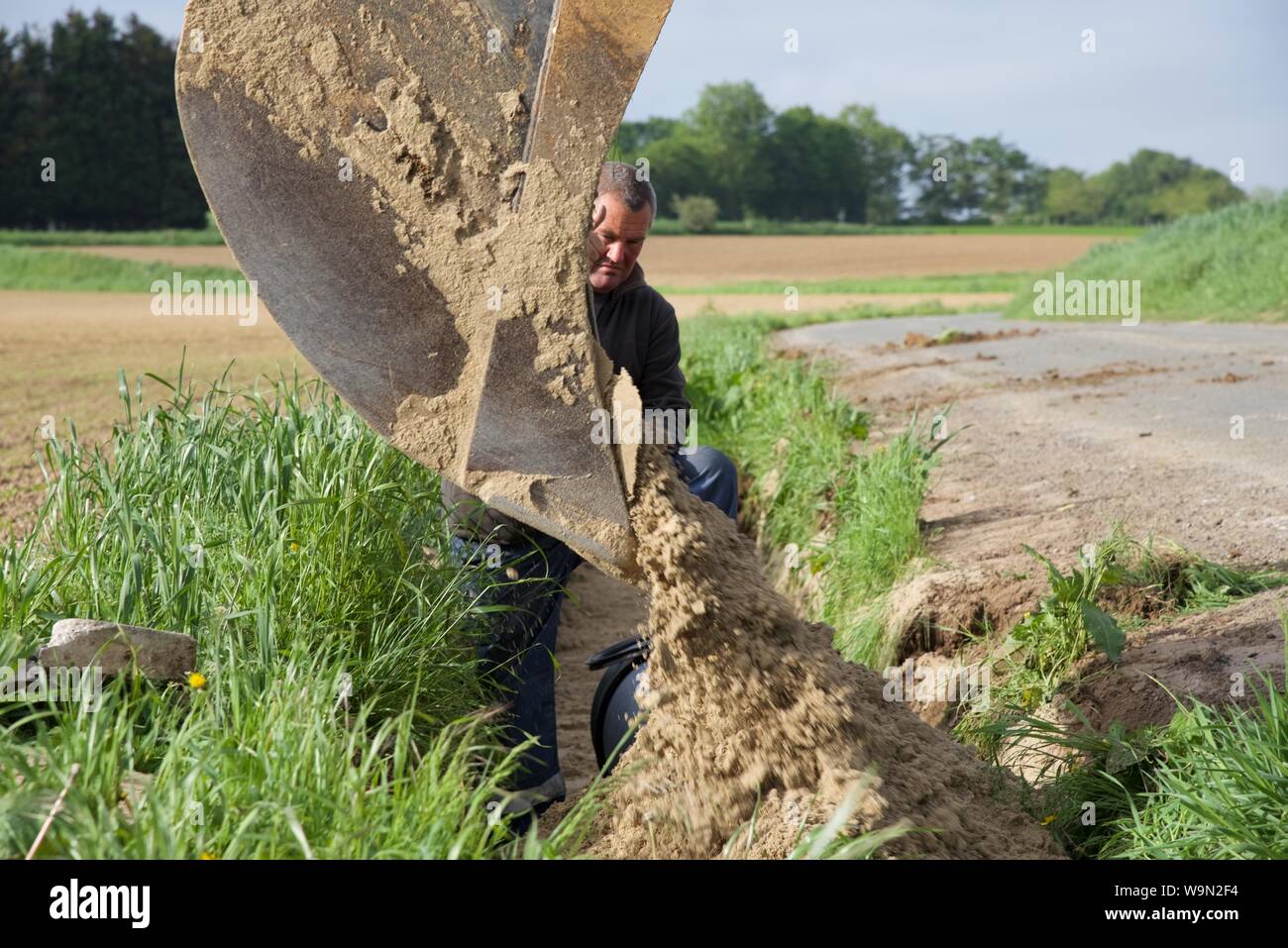 Ein Boden arbeitet Supervisor mit Handzeichen, der Baggerfahrer, wie Sie wieder ein Graben mit Sand füllen nach der Beerdigung einen Sturm Ablaufleitung Stockfoto