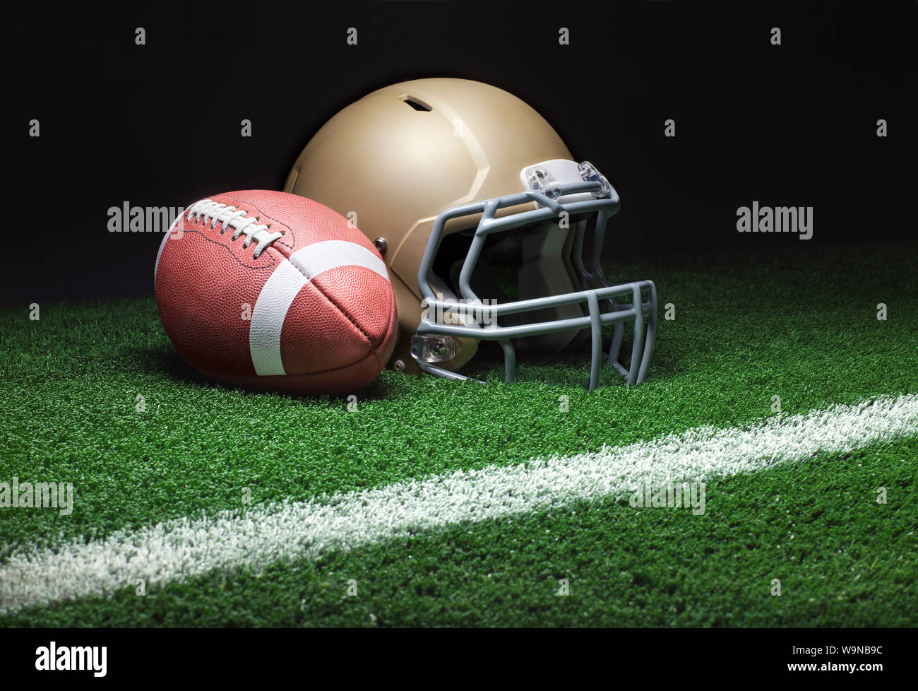 Ein niedriger Betrachtungswinkel von einer Gold football Helm mit einem Fußball auf eine Rasenfläche mit Streifen und dunklen Hintergrund Stockfoto