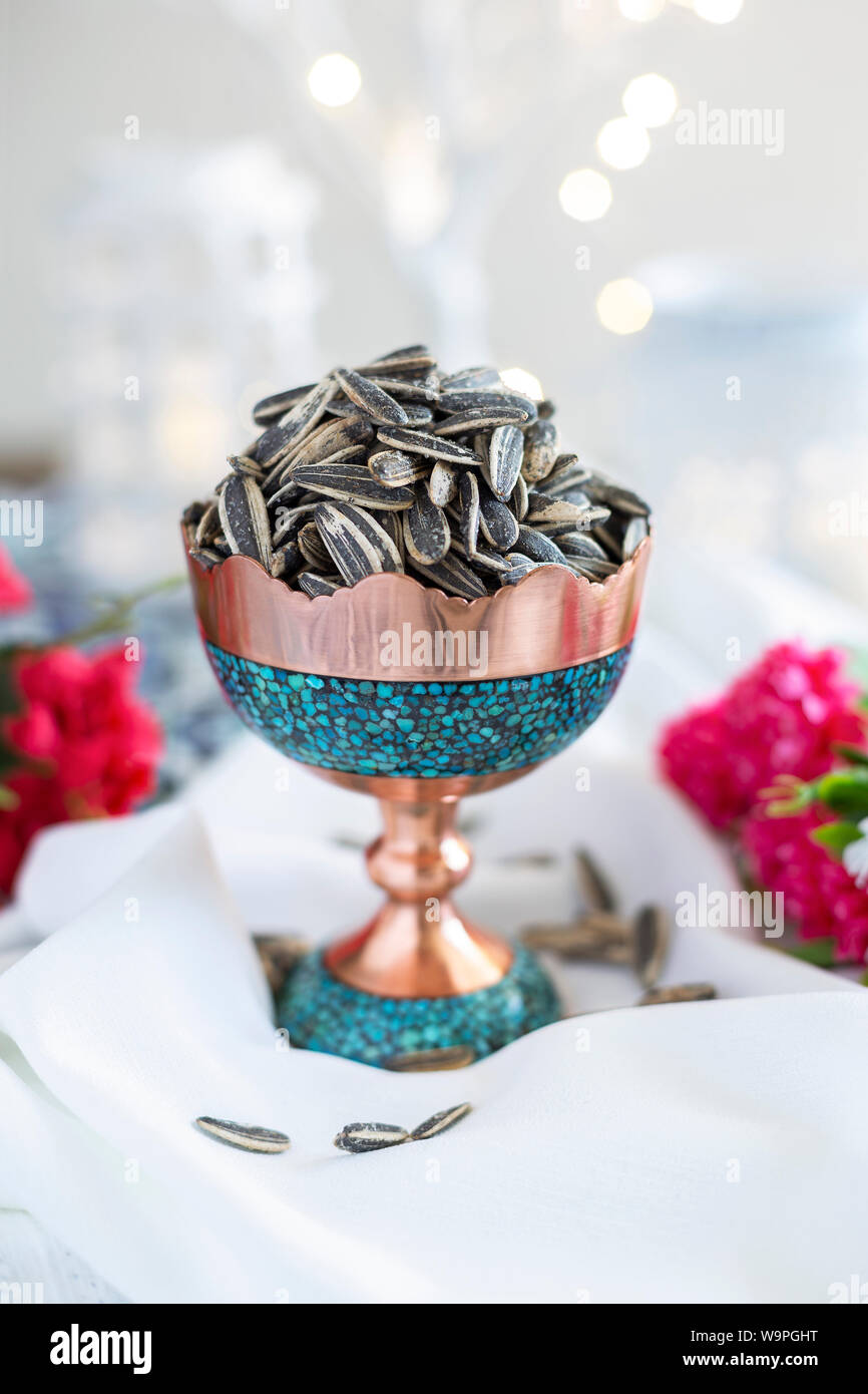 Eine Schüssel gefüllt mit Sonnenblumenkernen in einer wunderschönen türkisfarbenen und kupferfarbenen Schale, umgeben von Blumendekorationen. Stockfoto
