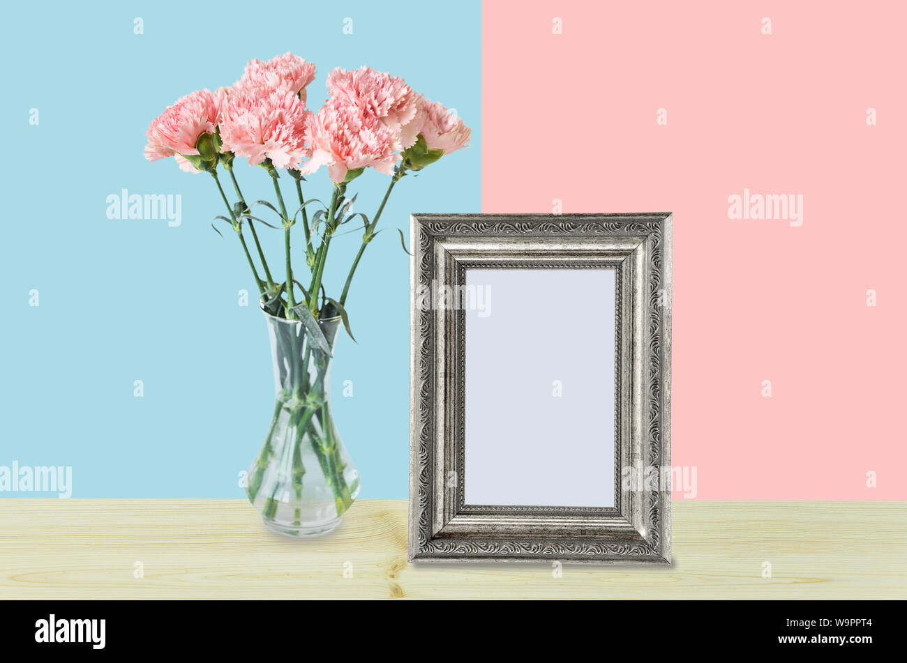 Home Decor mit einem leeren Silber Bilderrahmen und ein Blumenstrauß rosa Nelken in einem eleganten Glas Vase auf Rosa und blaue Hintergründe Stockfoto