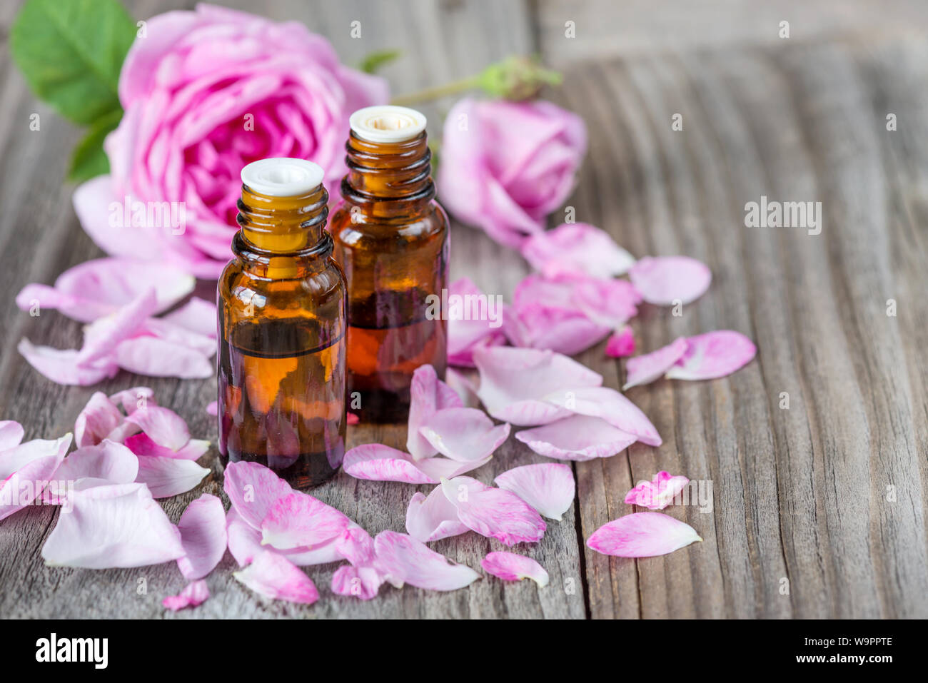 Zwei dunkle Durchstechflaschen mit Rose ätherisches Öl und Rosen auf einem hölzernen Hintergrund mit copy-Raum Stockfoto
