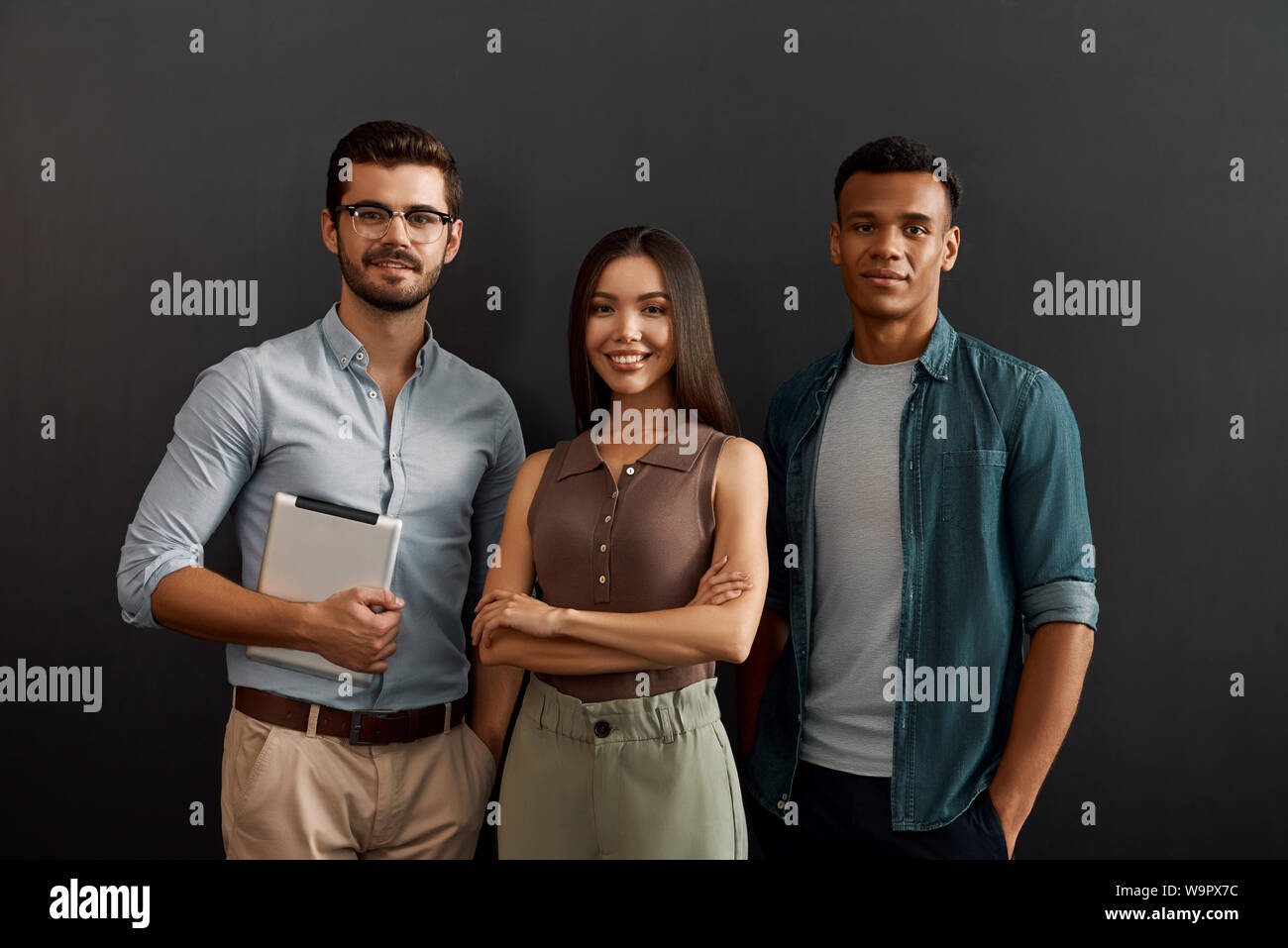 Perfekte IT-Team. Gruppe von drei fröhliche junge Menschen in Freizeitkleidung auf Kamera mit Lächeln, während gegen den dunklen Hintergrund stehen. Arbeit Konzept. Zusammenarbeit. Geschäftsleute Stockfoto