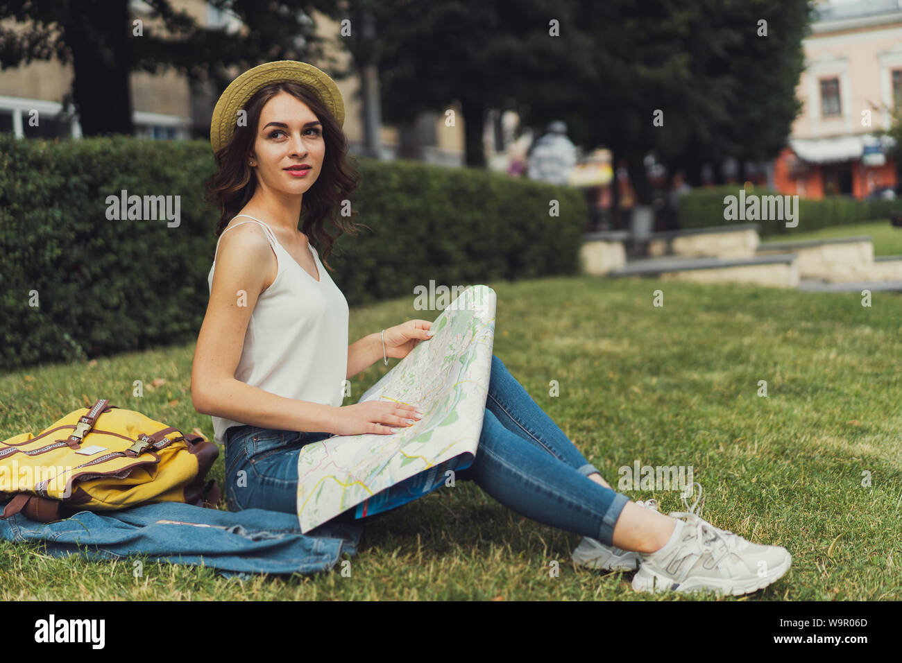 Schöne junge Frau sitzt auf Gras genießen Sie sonnige Tag im Park. Mit einem sanften Lächeln. Mit einer Karte in der Hand, konzentrierte sich auf etwas. Stockfoto