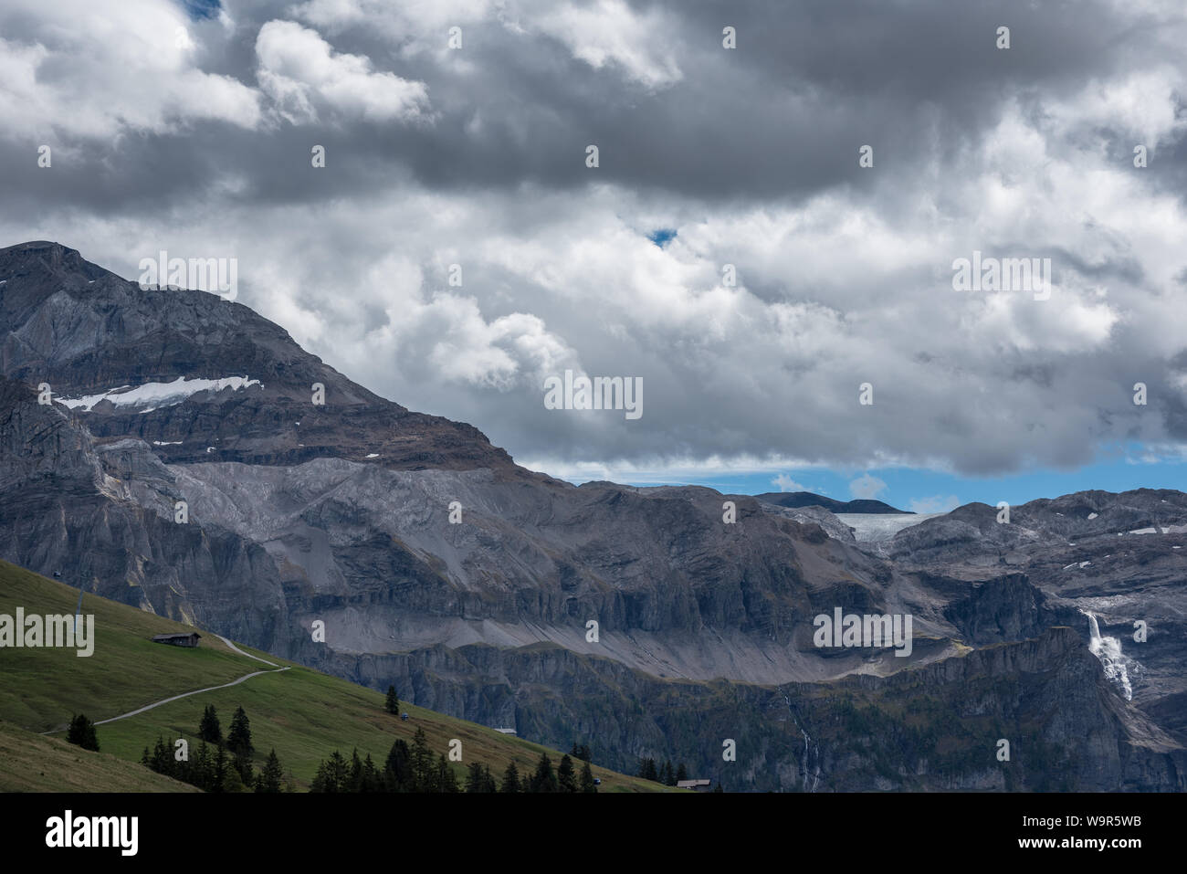 Blick vom Bühlberg/Lenk Wildstrubel Berge, Gletscher und Plaine-Morte Trübbachfall Wasserfall unter großen Wolken mit einem Streifen blauen Himmel Stockfoto