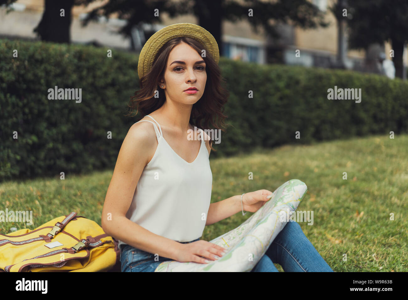 Schöne junge Frau sitzt auf Gras genießen Sie sonnige Tag im Park. Sommer glücklichen Moment. Mit einer Karte in der Hand, konzentrierte sich auf etwas. Stockfoto