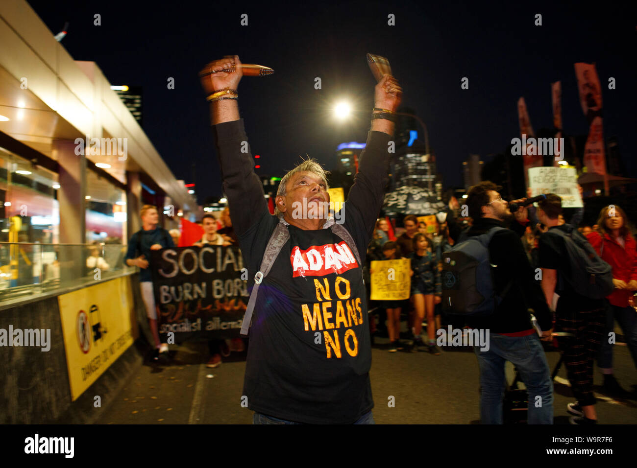 Indigene Menschen in Anti-Adani Coal Mine t-shirt spielt traditionelle Holz- Instrumente als er marschiert, über Victoria Brücke während Uni Studenten Arbeitsniederlegung Stockfoto