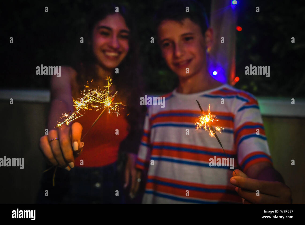 Junge Freunde, Party mit Feuerwerk im Freien auf der Terrasse. Lächelnde Mädchen und Jungen Spaß genießen Wunderkerzen bei Familie Geburtstag. Paar Bruder Stockfoto