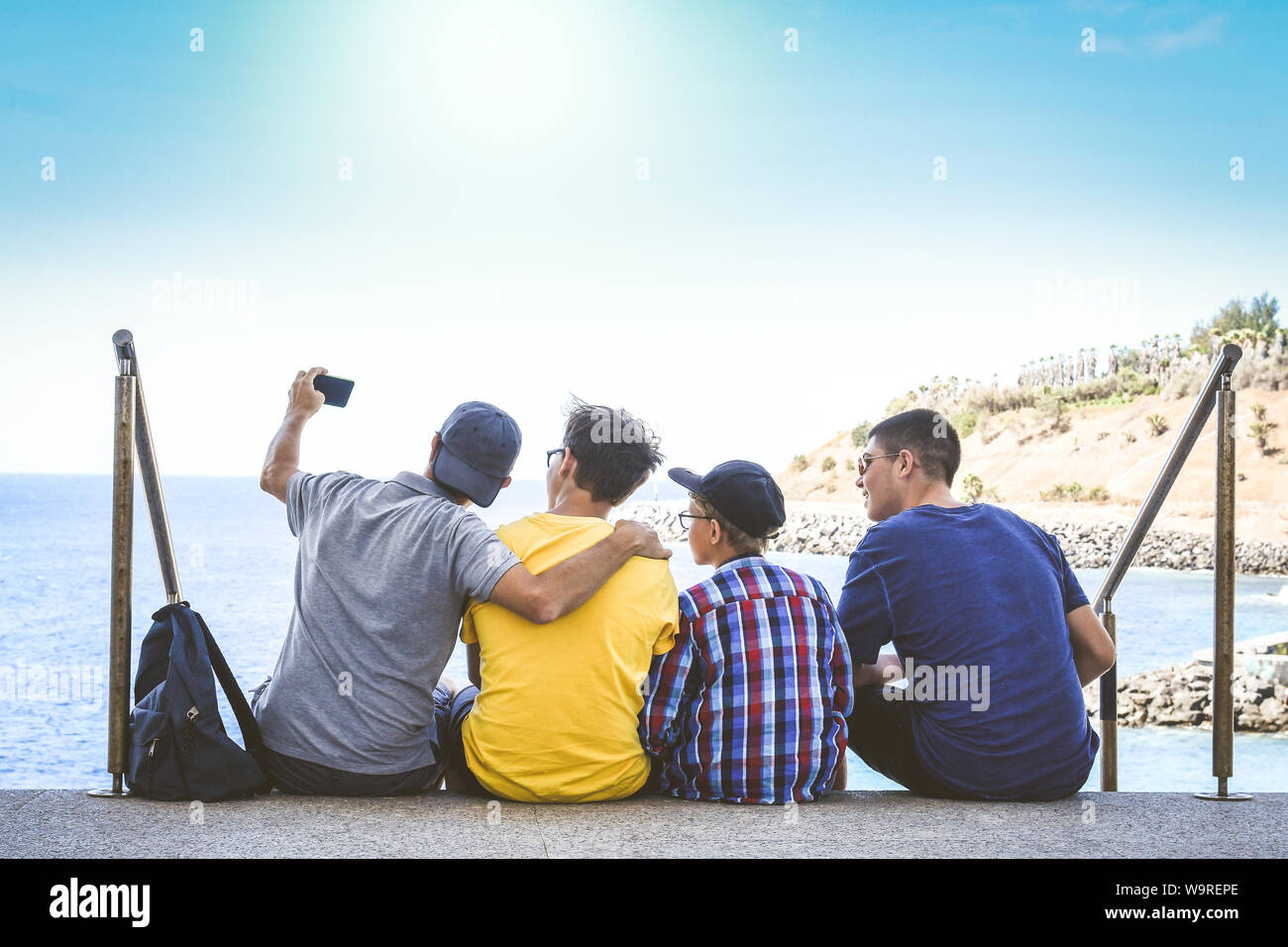 Zurück Blick auf die Gruppe der Jugendlichen, die selfie mit Smartphone. Vater und Söhne genießen Sie tropische Sommerferien. Blauer Himmel und Meer im Hintergrund. Stockfoto