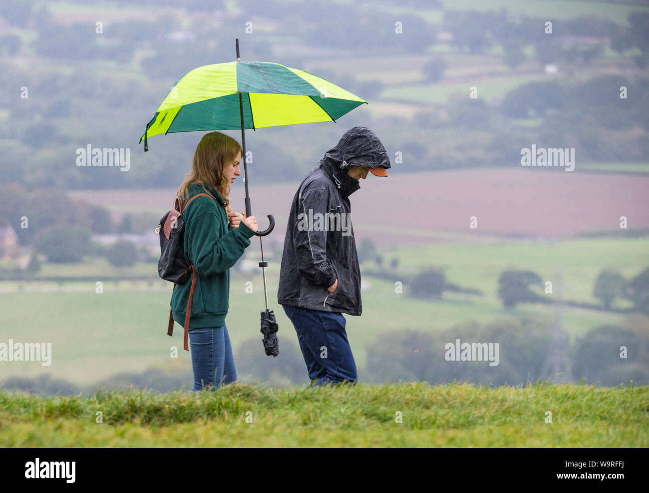 Junges Paar wandern im Regen mit Regenschirm. Ein nasses Wetter zu Fuß auf einem Hügel bei Regen an trüben Herbsttag im Vereinigten Königreich. Stockfoto