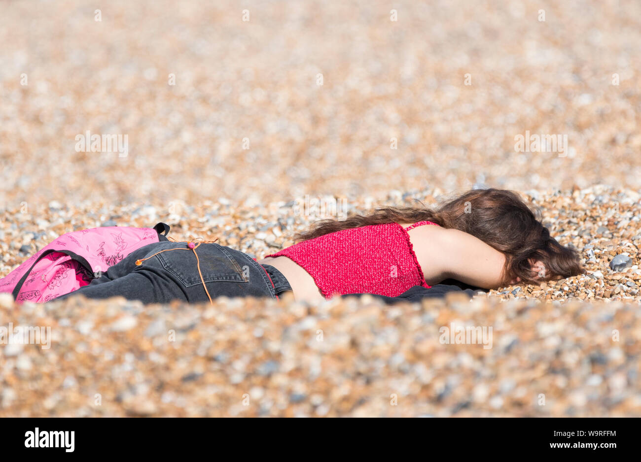 Junge Frau mit dem Gesicht nach unten im Kies am Strand in der Sonne. Junge weibliche Festlegung in der Sonne an einem warmen Frühlingstag in Großbritannien. Stockfoto