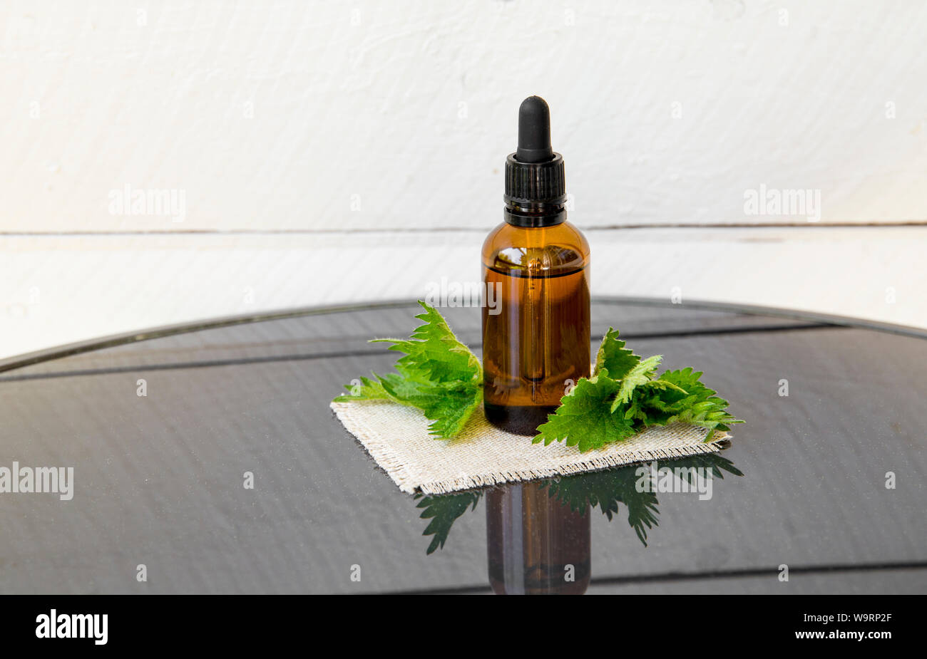 Nesseln ätherisches Öl oder Infusion in Braun Medical Pipettenflasche mit dekorativen Brennnessel Zweige Holzbrett Hintergrund. Stockfoto
