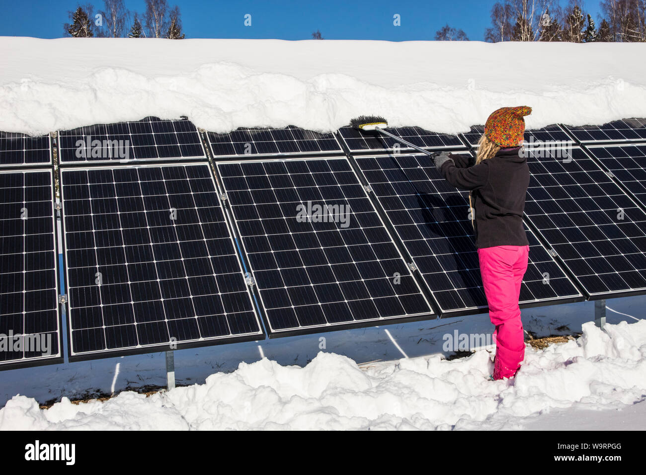 Frau schieben Schnee Solarmodule aus im Winter. Wenn Schnee Panels umfasst, können Sie nicht Strom erzeugen. Die kleinen privaten Home Haus im Hintergrund. Stockfoto