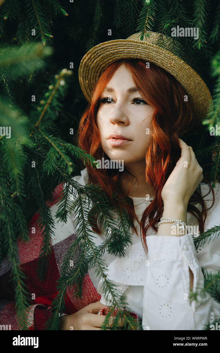 Rothaarige schöne Mädchen in einem Strohhut in Kiefer posing und firebranches Outdoor Stockfoto